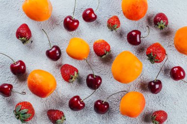 Beton arka plan üzerinde çeşitli taze yaz meyveleri. Çilek, kiraz ve kayısı. Üst görünüm, düz yatıyordu