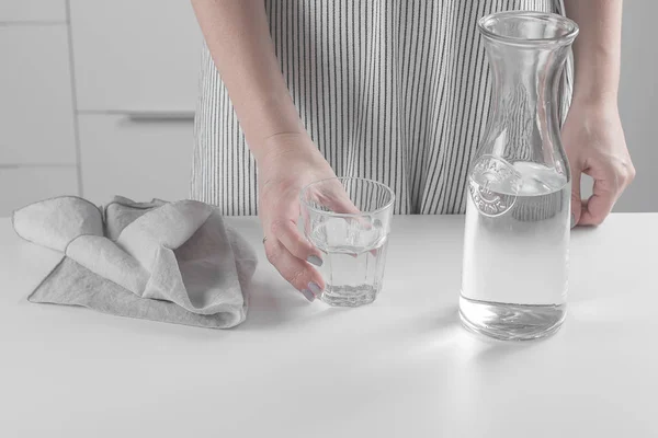 Mujer sosteniendo un vaso de agua pura. Jarra de botella grande en la mesa de la cocina. Concepto limpio — Foto de Stock