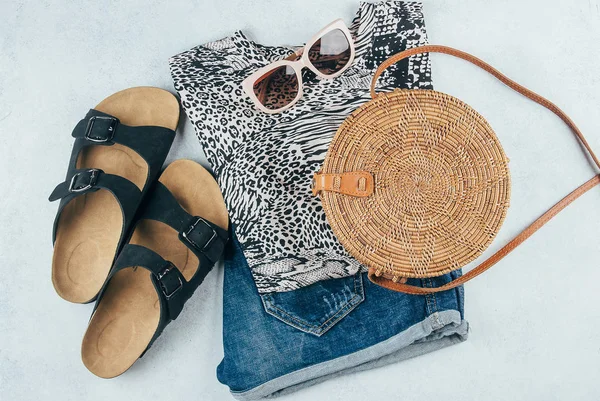 Flat lay with summer women's clothing and accessories. Animal print t-shirt, blue denim shorts, fashionable organic rattan bag, sunglasses. Vacation, travel concept. Top view — Stock Photo, Image