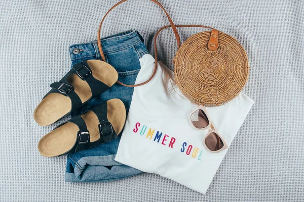 Flat lay with summer women's clothing and accessories. White t-shirt, blue denim shorts, fashionable organic rattan bag, sunglasses. Vacation, travel concept. Top view — Stock Photo, Image