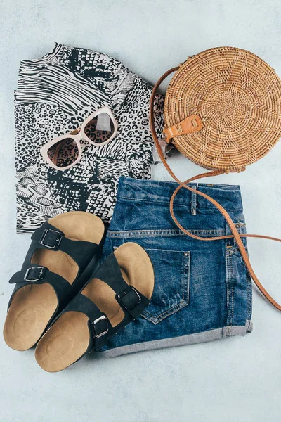 Flat lay with summer women's clothing and accessories. Animal print t-shirt, blue denim shorts, fashionable organic rattan bag, sunglasses. Vacation, travel concept. Top view — Stock Photo, Image