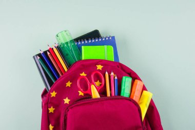 Pastel yeşil arka plan üzerinde farklı renkli kırtasiye ile Kırmızı sırt çantası. Okul konseptine geri dönelim. Üst görünüm, kopyalama alanı