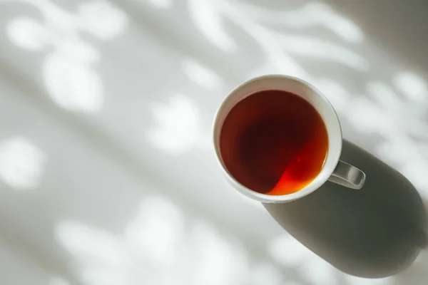 Tazza di tè bianco su sfondo astratto di ombra tenda naturale che cade sul tavolo bianco. Bianco e nero tono monocromatico — Foto Stock