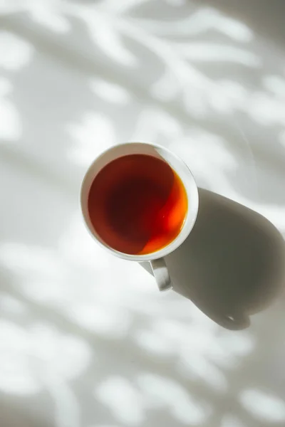 White cup of tea on abstract background of natural curtain shadow falling on white table. Black and white monochrome tone