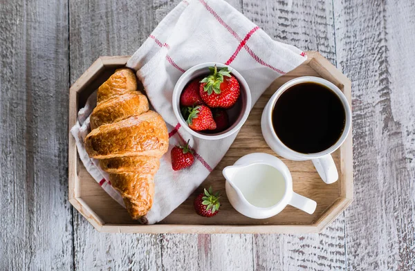 Concepto de desayuno. Taza de café, croissants recién horneados y fresa fresca en bandeja de madera. Fondo de tabla de madera. Vista superior, espacio de copia . — Foto de Stock