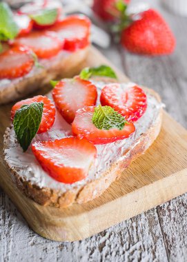 Masa arka planda ahşap tahta üzerinde krem-peynir üzerinde çilek ve nane ile iki tost veya Bruschetta. Close