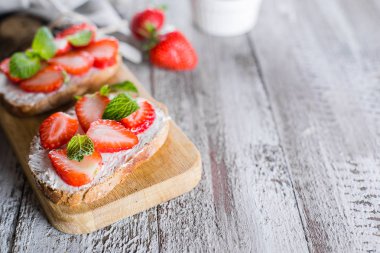 Masa arka planda ahşap tahta üzerinde krem-peynir üzerinde çilek ve nane ile iki tost veya Bruschetta. Boşluk Kopyala