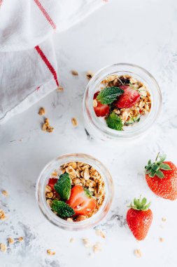 Beyaz mermer masa üzerinde granola, çilek ve yoğurt yapılmış lezzetli parfaits ile iki kavanoz, üst görünüm
