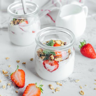 Beyaz mermer masada granola, çilek ve yoğurt yapılmış lezzetli parfaits ile iki kavanoz