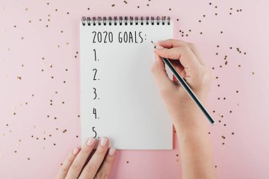 Mutlu Yıllar 2020. Kadın el yazma 2020 Pembe arka plan üzerinde Noel süslemeleri ile süslenmiş deftergol. Üst görünüm, düz yatıyordu