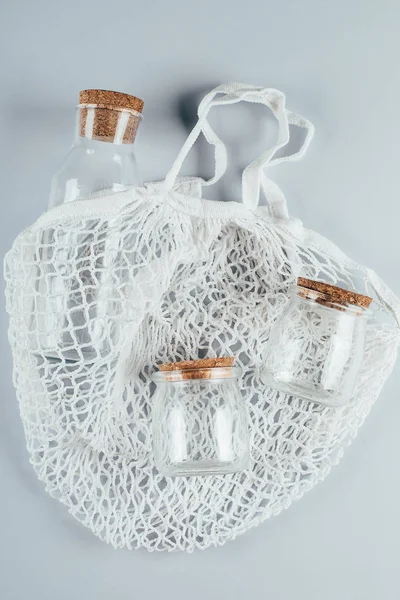 Zero Waste, milieuvriendelijk concept. Mesh tas met glazen potten en fles op grijze achtergrond. Bovenaanzicht, vlakke lay — Stockfoto