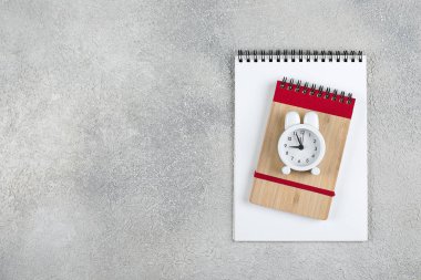 Okula geri dön. Okul zamanı minimal kavramı. Not defteri, kalem, gri beton arka plan üzerinde çalar saat. Düz döşeme, üst görünüm