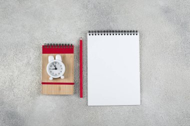 Okula geri dönelim sahte konsept. Okul zamanı minimal kavramı. Not defteri, kalem, gri beton arka plan üzerinde çalar saat. Düz döşeme, üst görünüm, kopyalama alanı