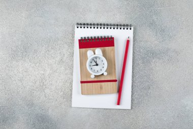 Okula geri dön. Okul zamanı minimal kavramı. Not defteri, kalem, gri beton arka plan üzerinde çalar saat. Düz döşeme, üst görünüm