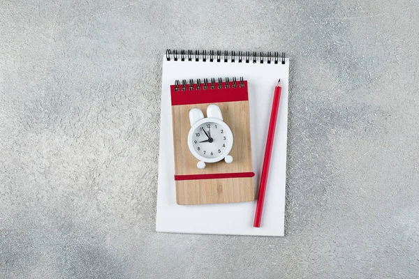 Okula geri dön. Okul zamanı minimal kavramı. Not defteri, kalem, gri beton arka plan üzerinde çalar saat. Düz döşeme, üst görünüm