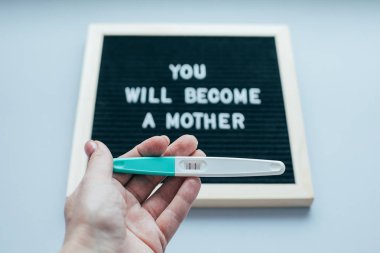 Kadın elinde pozitif pregnan ile gebelik testi. Kopya alanı. Mesaj panosu ile metin Bir anne olacak