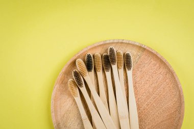 Gri arkaplanda tahta tabakta bambu diş fırçasıyla düz bir kompozisyon vardı. Çevresel bambu diş fırçaları. Sıfır atık, plastik madde konsepti. Üst görünüm, alanı kopyala
