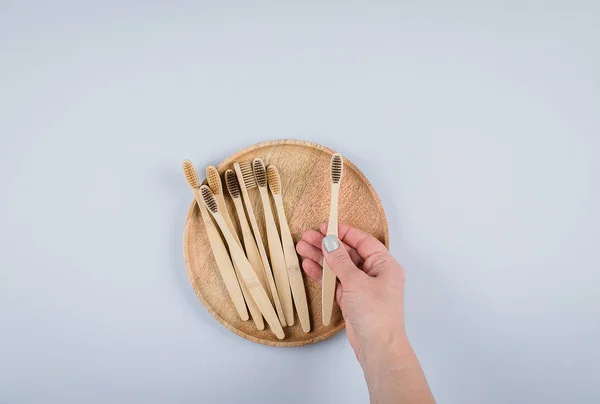 Плоская композиция с бамбуковыми зубными щетками на деревянной пластине на сером фоне. Эко натуральные бамбуковые зубные щетки. Понятие отходов, вещей без пластика. Вид сверху, пространство для копирования — стоковое фото