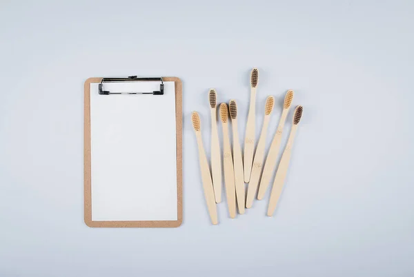 Vlakke lay compositie met bamboe tandenborstels en lege witte notitieblok blanco voor tekst op grijze achtergrond. Eco natuurlijke bamboe tandenborstels. Geen afval, plastic vrije items concept. Bovenaanzicht, kopieer ruimte — Stockfoto