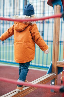 Çocuk 5 yaşında, çocuk parkında turuncu ceketli. Çocukların dışarıda boş zamanı, sokaklarda oyunlar..