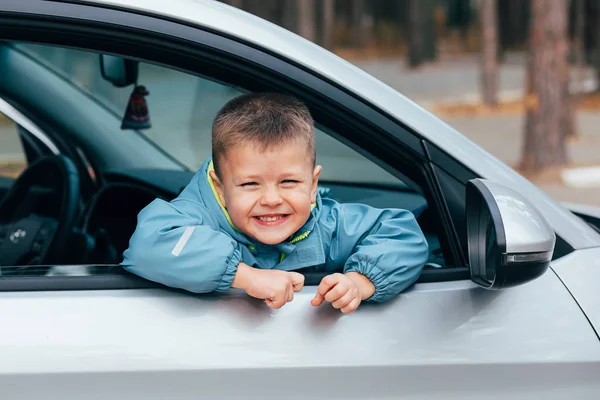 Lindo niño con una chaqueta azul viajando en el coche y mirando por la ventana y oliendo. Concepto de viaje —  Fotos de Stock