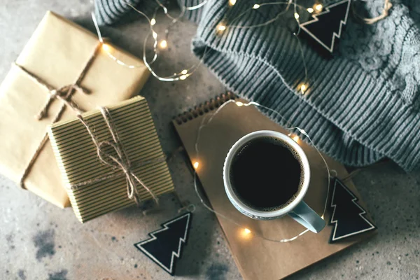 Accogliente composizione invernale con una tazza di caffè, scatola regalo, regali, maglione e luci ghirlanda. Natale o Capodanno 2020 concetto di vacanza. Accogliente, umore, stile di vita, natura morta — Foto Stock