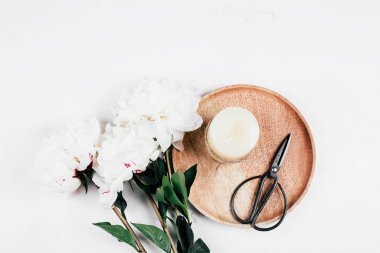 Beyaz şakayık ve ahşap tepside mum, beyaz arka planda makas. Samimi, sakin bir hayat, asgari konsept. Üst görünüm, düz görünüm, kopyalama alanı