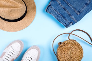 Mavi kot şort, spor ayakkabı, şapka ve mavi arka planda modern rattan çanta. Düz konum, üst görünüm, kopyalama alanı. Yaz kıyafeti konsepti