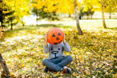 Çocuk sonbahar arka planında el yapımı balkabağı ile yüzünü kapatıyor. Cadılar Bayramı konsepti.