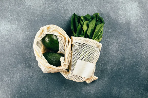 Avocado and spinach in eco cotton bags on table. Zero waste shopping concept. Flat lay, top view.