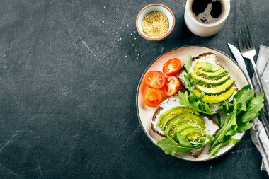 Süzme peynirli avokado tostları, roka, koyu masada bir fincan kahve. Sağlıklı kahvaltı, atıştırmalık. Üst görünüm, alanı kopyala