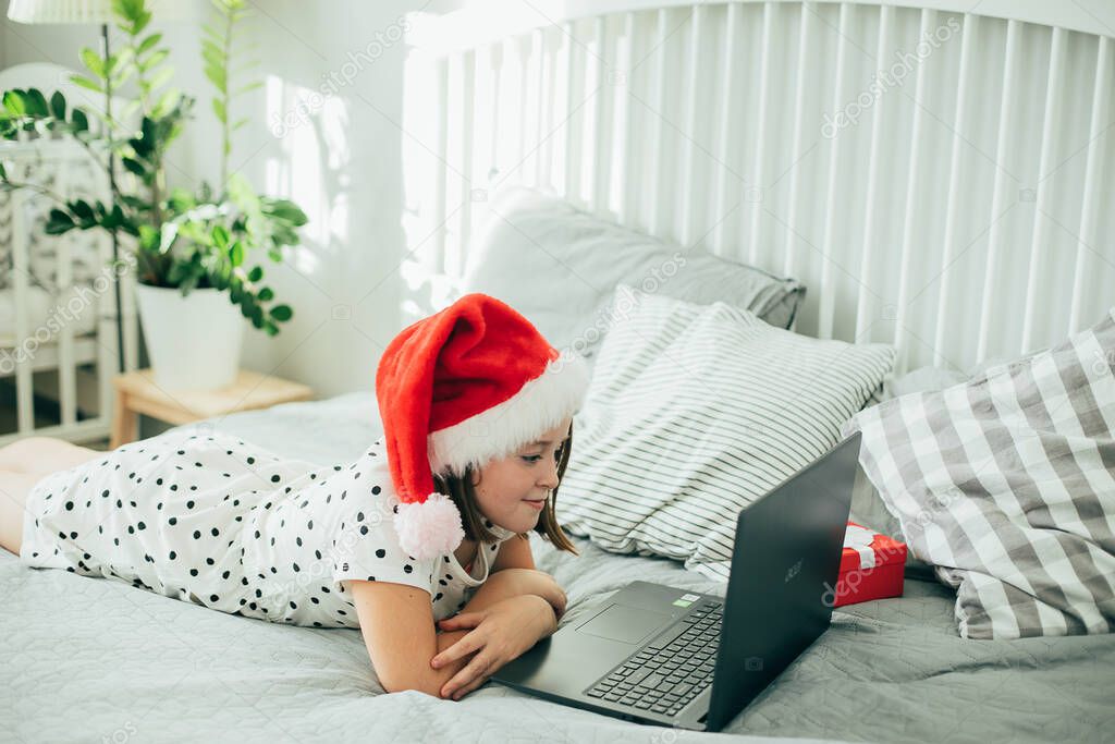 Girl in a hat of Santa Claus celebrates with family holiday of Christmas. COVID holiday, social distancing, online holiday concept