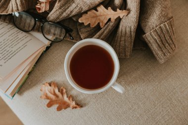 Sonbahar konsepti. Düz bej örgü süveter, bir fincan çay, açık kitap ve kuru meşe yaprakları..
