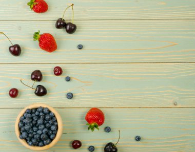 Taze güzel çilek, kiraz ve ürün montajı için eski vintage ahşap arka plan üzerinde yaban mersini. Mavi ahşap masa Danışma Kurulu doku ile kopya alanı ile olgun orman meyveleri üstten görünüm