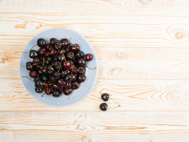 Taze kırmızı kiraz kopya alanı tasarım montaj veya mockup eski ahşap zemin üzerine mavi tabak. Rustik ahşap masa Danışma Kurulu doku ile yığın tatlı kiraz kadar yakın ve görünümü ana sayfa