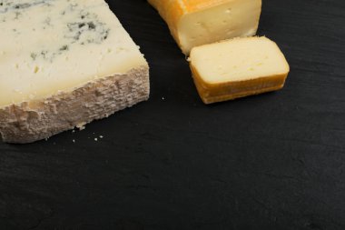 Peygamberli dilimlenmiş Limburger, Herve peynir veya Reblochon ve mavi Gorgonzola, rokfor veya Stilton. Peynir siyah sarı ve mavi peynir üstten görünüm karışımı ile ders taş plaka arka plan