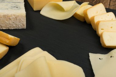 Peygamberli dilimlenmiş Limburger, Herve peynir veya Reblochon ve mavi Gorgonzola, rokfor veya Stilton. Peynir siyah sarı ve mavi peynir üstten görünüm karışımı ile ders taş plaka arka plan