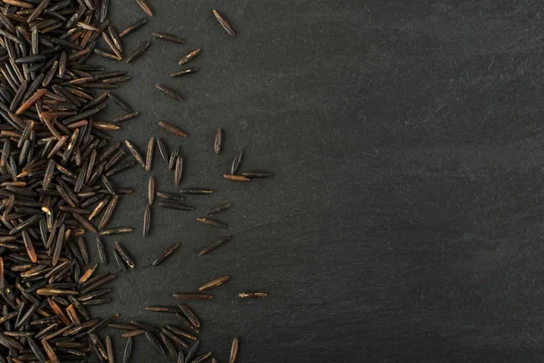 Ham siyah yabani pirinç üzerinde koyu taş arka plan en iyi görünüm düz yatıyordu. Sağlıklı diyet Kanada Bio pirinç tahıl doku TOPVIEW metin veya boşaltmak için yer ile