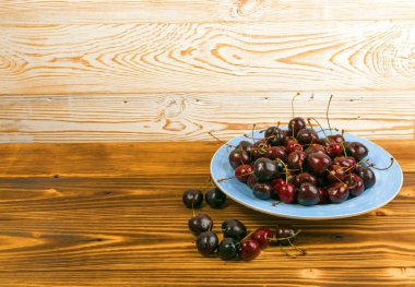 Yuvarlak mavi tabak taze olgun kiraz tasarım montajı için eski ahşap zemin üzerinde. Antika ahşap masa Danışma Kurulu ile olgunlaşmış kiraz veya tatlı çilek kazık kopya alanı ile yakından