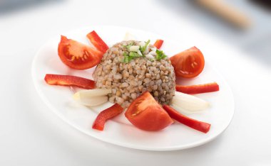 Mükemmel hizmet Buğday lapası beyaz tabakta. Rus kaşa veya pişmiş Pseudocereal Buck buğday domates, soğan ve Yeşiller ile dekore edilmiş