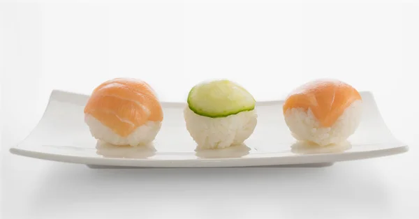 少しの握り寿司やサーモンとキュウリを明るい背景の手鞠をクローズ アップ 白い皿に赤い刺身でおにぎり — ストック写真