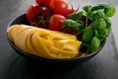 Çiğ sarı İtalyan makarna pappardelle, fettuccine veya tagliatelle yakın çekim. Ev yapımı kuru erişte, uzun rulo makarna ya da domatesli pişmemiş makarna ve fesleğen.