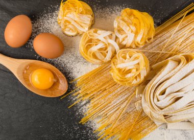 Çiğ sarı İtalyan makarna pappardelle, fettuccine veya tagliatelle yumurta ile kapatın. Ev yapımı yumurta pişirme işlemi, uzun Hadde makarna veya siyah taş zemin üstten görünüm üzerinde pişmemiş makarna erişte