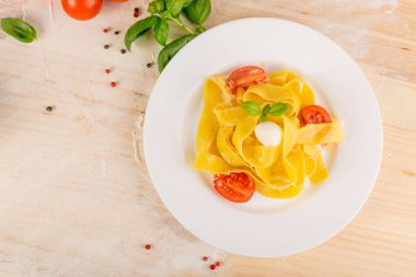 Sarı pişmiş makarna pappardelle, fettuccine veya beyaz tabak üstten görünüm üzerinde tagliatelle. Ahşap rustik arka plan üzerinde yumurta ev yapımı şerit erişte veya makarna domates, fesleğen ve mozzarella ile topları