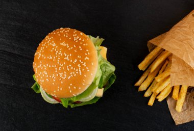 Klasik Burger taze soğan, yeşillik, peynir ve patates kızartması garnitür üstten görünüm. Hamburger ya da doğal siyah taş zemin üzerine Chickenburger