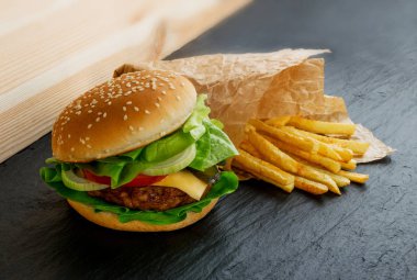 Soğan, yeşillik, peynir ve patates kızartması garnitür ile klasik taze Burger kapatın. Hamburger ya da doğal siyah taş zemin üzerine Chickenburger