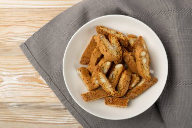 Biscotti di prato 'nun rustik masa örtüsü çuval bezi arka planı. Geleneksel İtalyan fındık kurabiyeleri. Beyaz tabakta bademli ev yapımı cantucci kurabiyesi.