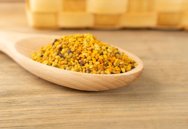 Arı poleninin makro çekimi ya da bulanık kırsal arka planda tahta kaşıkta perga. Çiğ kahverengi, sarı, turuncu ve mavi polen taneleri veya arı ekmeği. Seçici odaklı sağlıklı gıda takviyesi