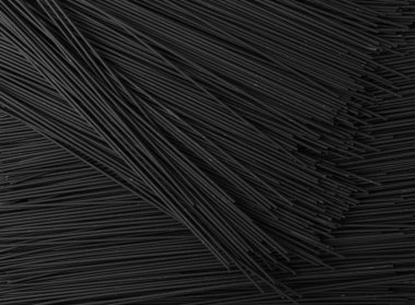 Siyah arka planda çiğ ev yapımı spagetti maketi. Kuru siyah erişte dokusu, makarna deseni. Koyu tenli İtalyan spagetti manzaralı.