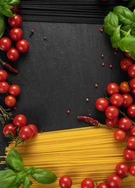 Koyu arkaplanda fotokopi alanı olan çiğ ev yapımı spagetti. Kuru siyah erişte, sarı makarna, kiraz domatesleri, yeşil fesleğen. Pişmemiş İtalyan spagetti manzarası